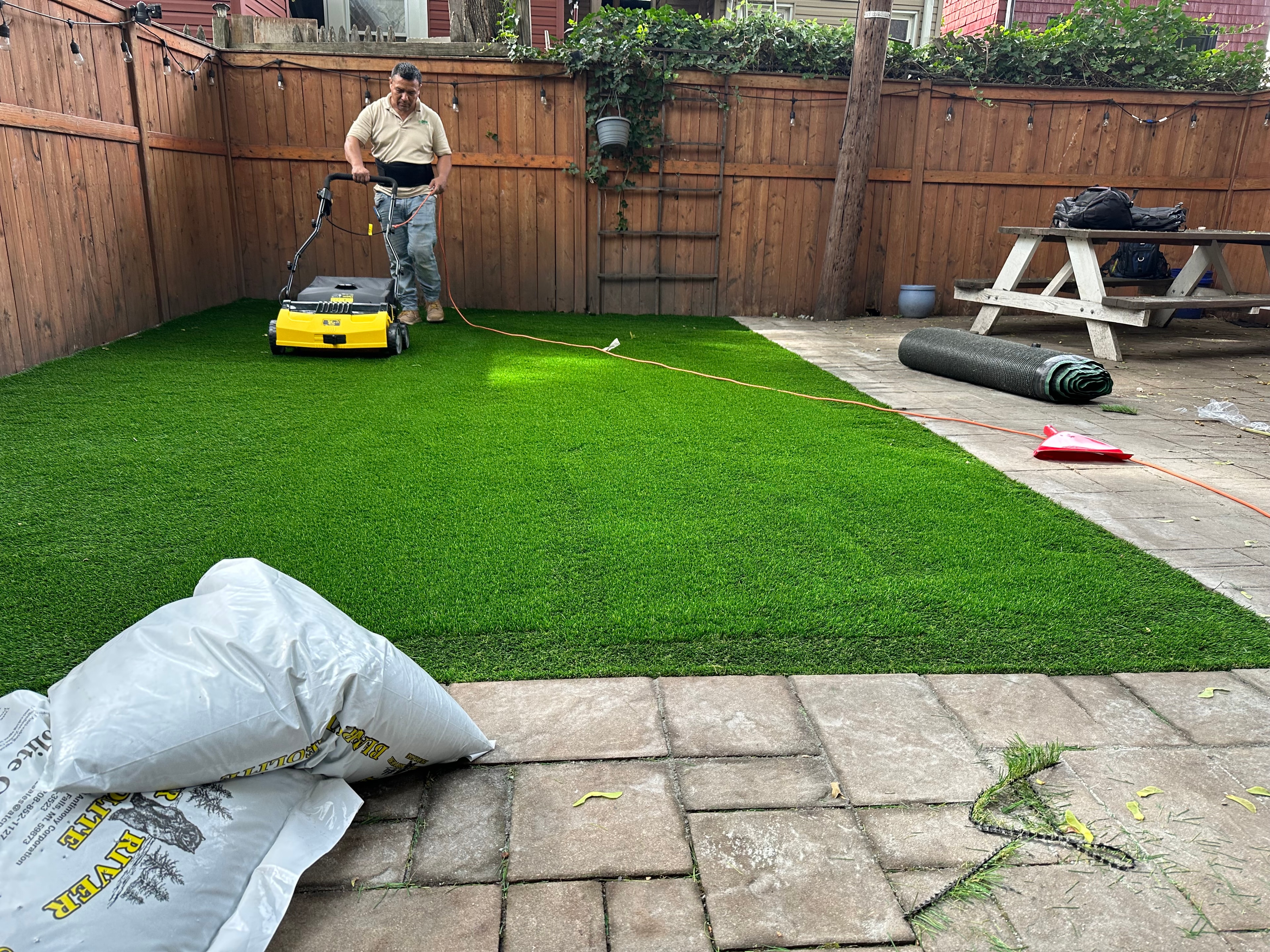 Worker using power broom to brush infill into artificial turf during installation