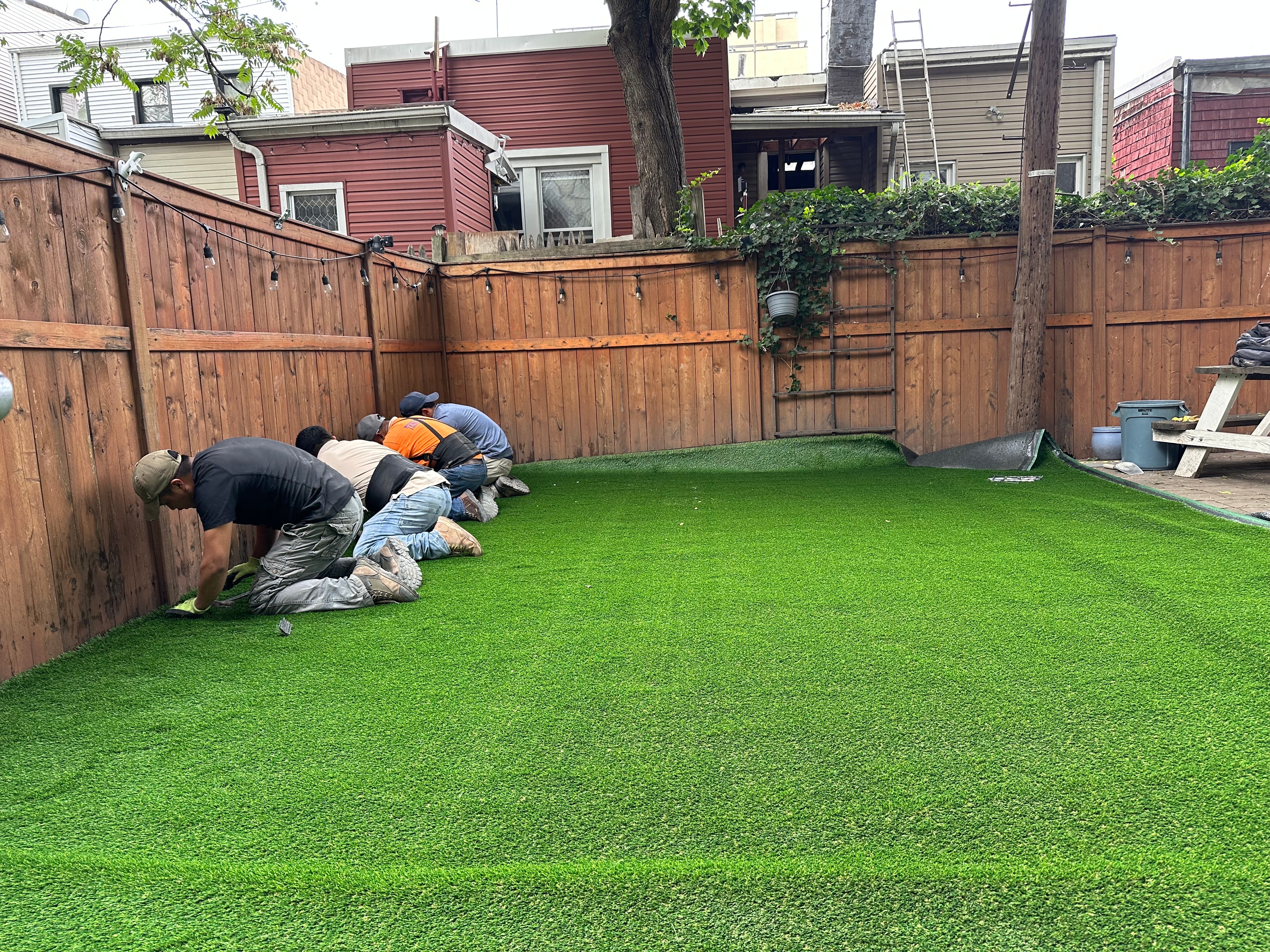 JKPOH crew laying and seaming artificial turf across residential backyard