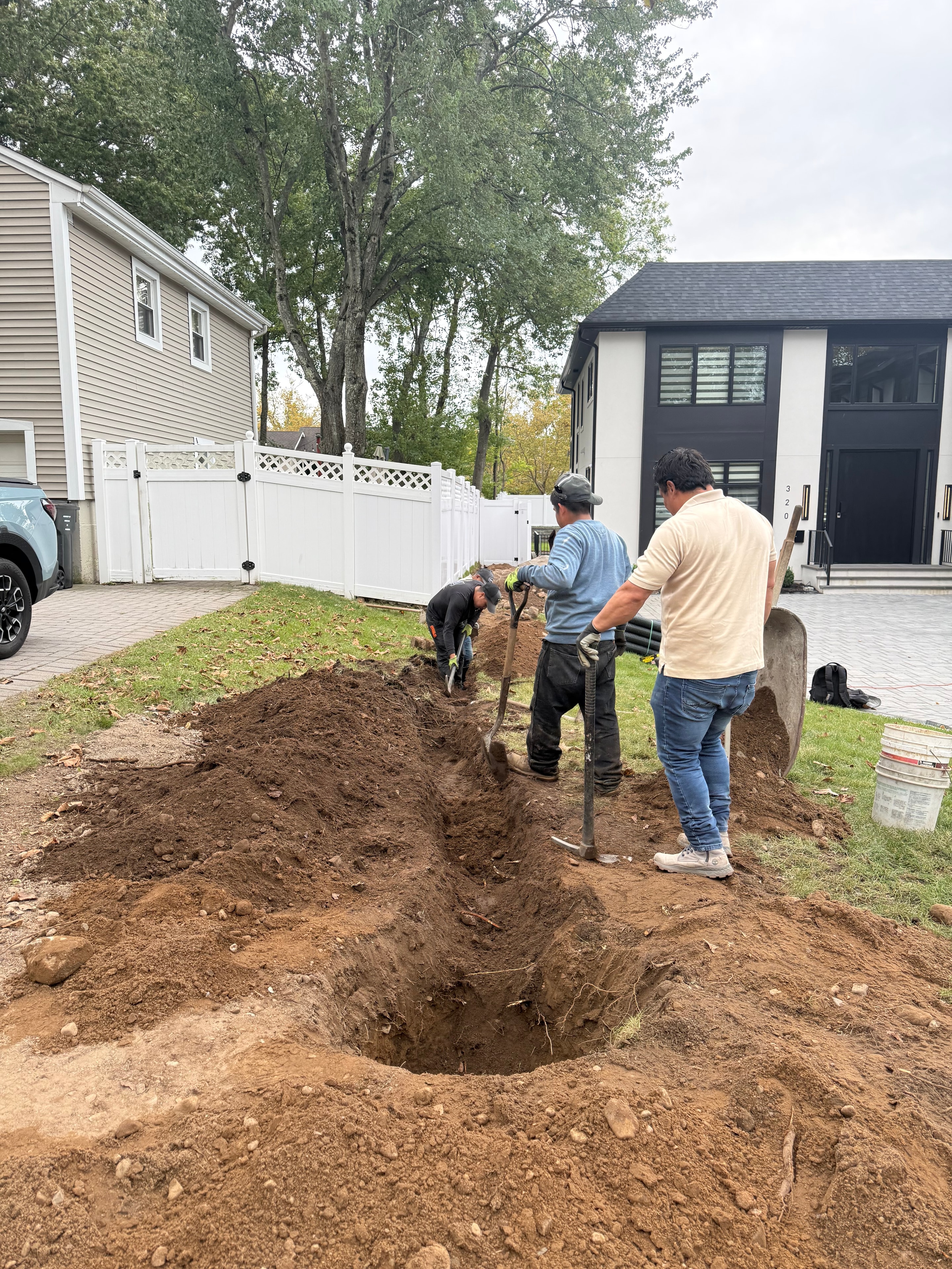 JKPOH Exterior Group crew hand-excavating drainage trench at a residential property in Paramus, NJ — work in progress